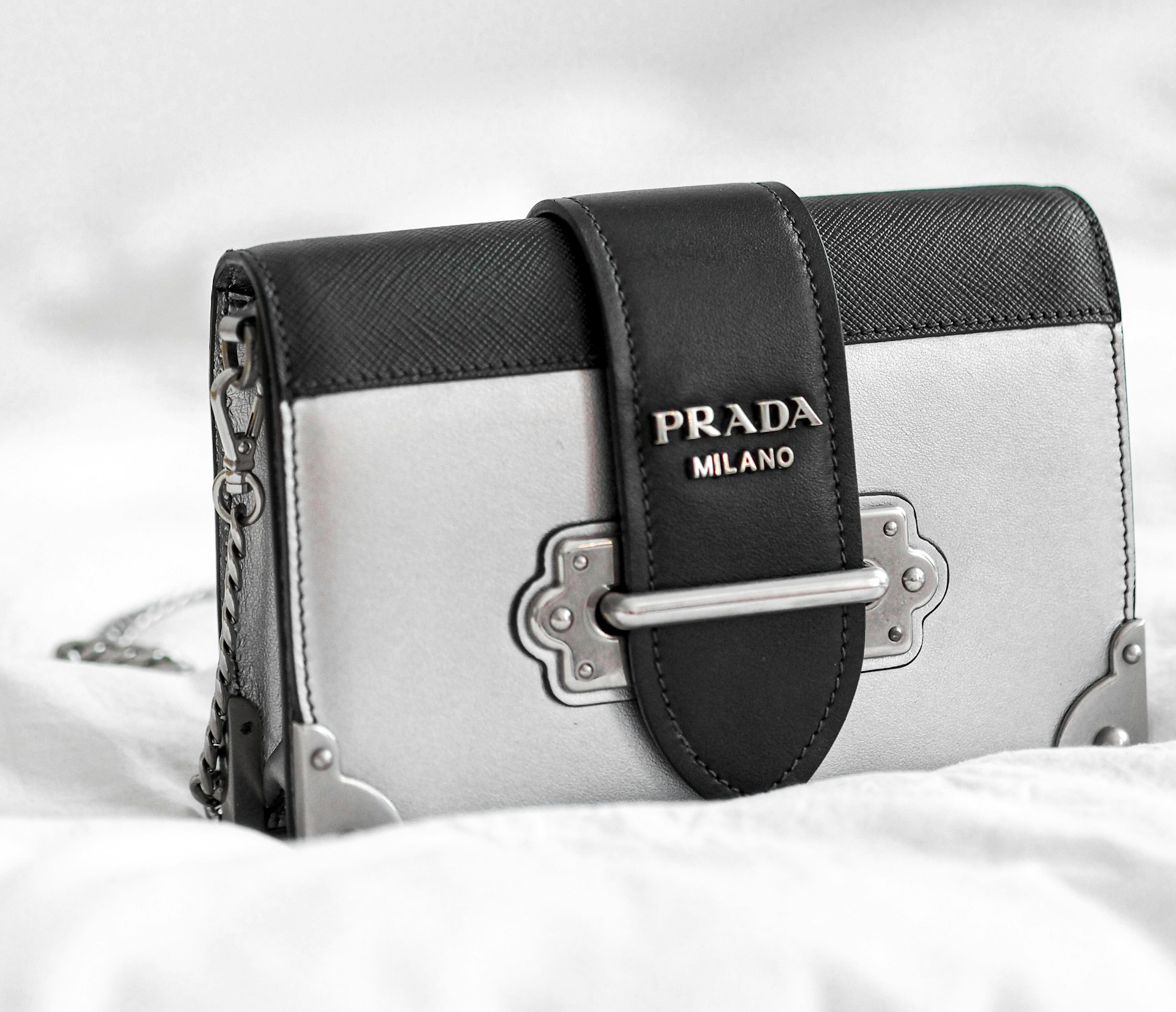 A Prada Milano handbag with a black strap and metallic clasp sits on a white surface.