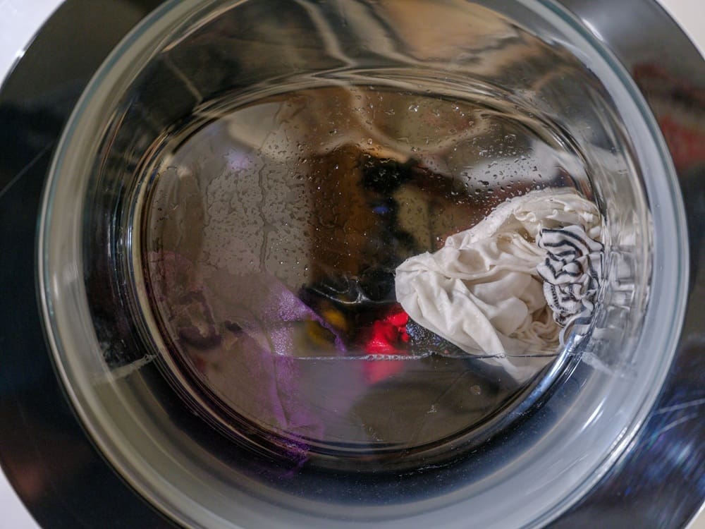 Close-up view of a washing machine drum with a few pieces of light-colored clothing inside and condensation on the glass door.