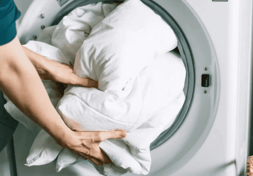 Person placing a large white comforter into the front-loading washing machine.