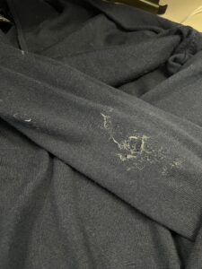 A close-up of a dark fabric with visible lint or pet hair scattered on the surface.