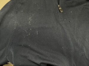 A close-up of a dark fabric with visible white lint and a small zipper.