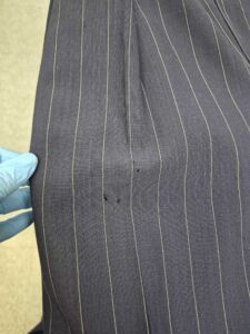 A close-up of a pinstriped fabric with small holes, held by a person wearing a blue glove.